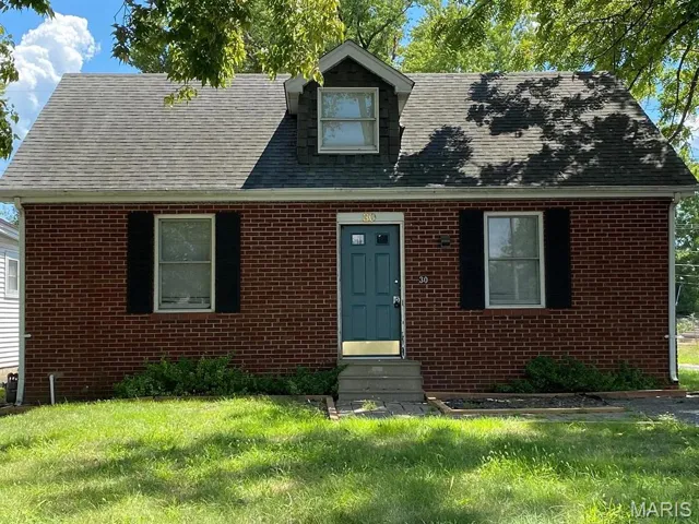 Cape cod-style house featuring roof with shingles, a front yard, and brick siding