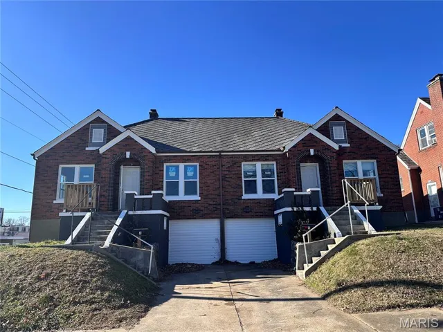 View of front facade with brick siding, a chimney, and driveway