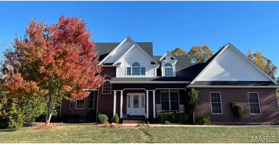 Traditional home with covered porch, a front yard, and brick siding