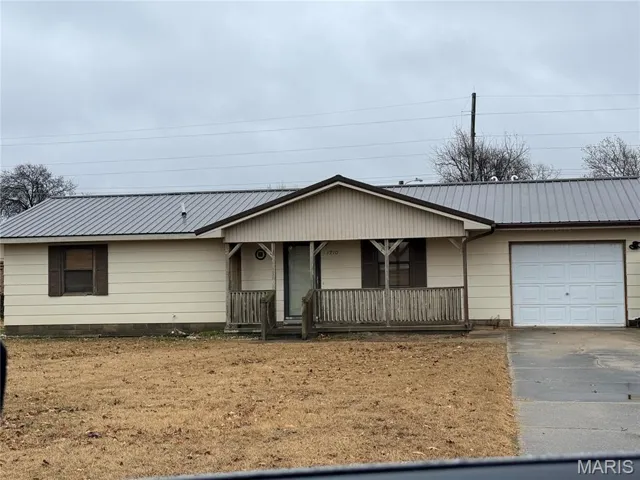 Ranch-style house featuring a metal roof, covered porch, driveway, and a garage