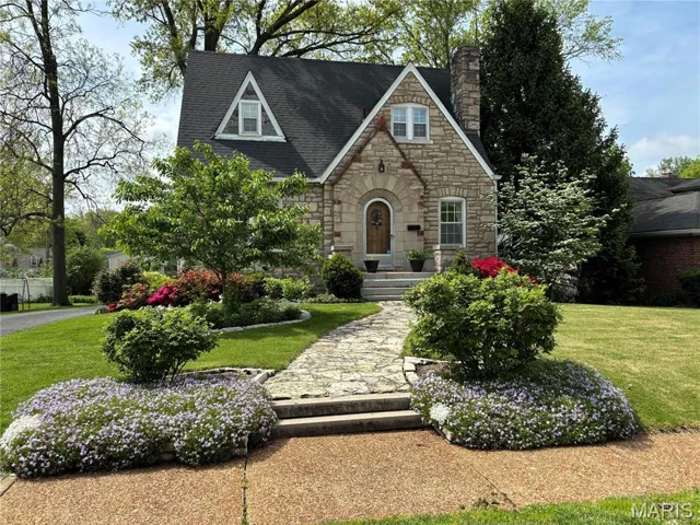 Charming stone cottage featuring an arched entry and timeless architectural details. Beautifully landscaped grounds with a stone walkway and vibrant flowering beds offer exceptional curb appeal.