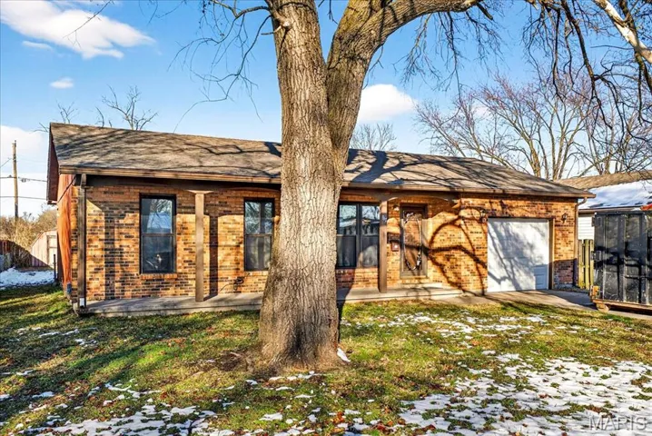 Snow covered property with brick siding, a shingled roof, a lawn, and covered porch