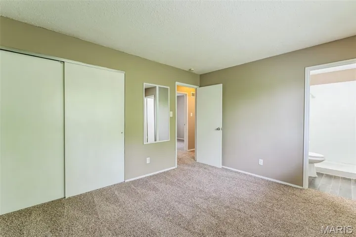 Unfurnished bedroom featuring a textured ceiling, carpet, a closet, and connected bathroom