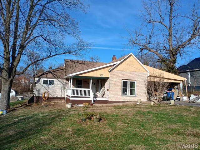 View of front of house with a chimney, a front lawn, a porch, and an attached carport
