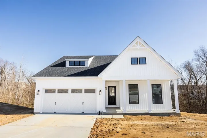 Modern farmhouse featuring a porch, driveway, and an attached garage