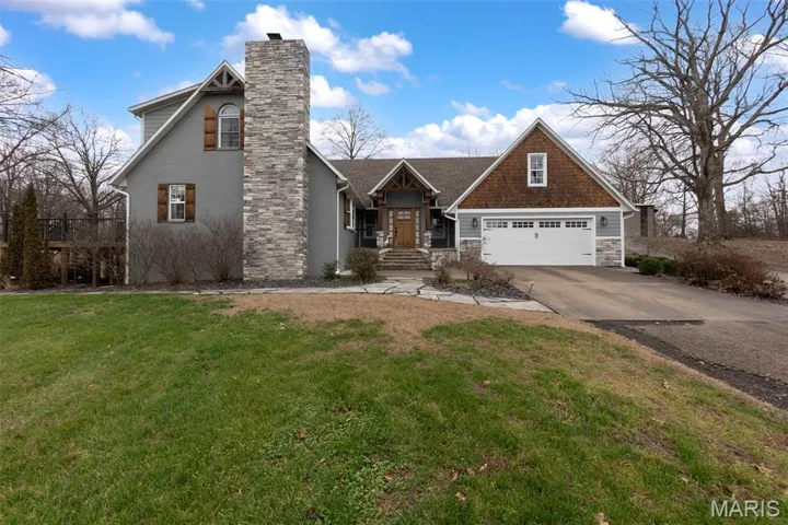 View of front facade featuring stone siding, a chimney, concrete driveway, a garage, and a front lawn