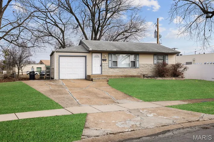 View of front facade featuring concrete driveway, roof with shingles, an attached garage, and stone siding