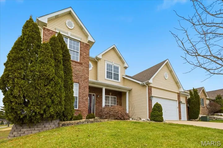 Traditional-style house featuring brick siding, a front lawn, concrete driveway, and covered porch