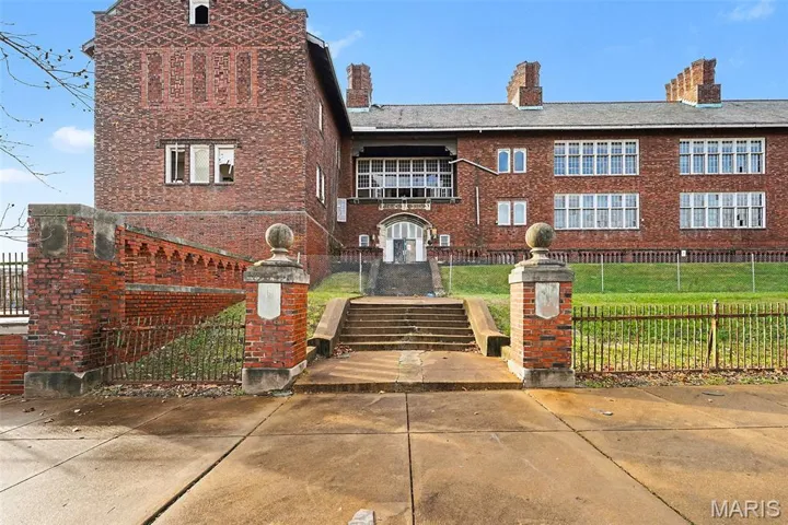 View of front of house featuring a fenced front yard, a chimney, brick siding, a balcony, and a gate