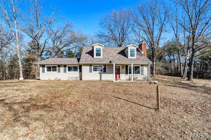 New england style home featuring covered porch, a chimney, roof with shingles, and a front lawn