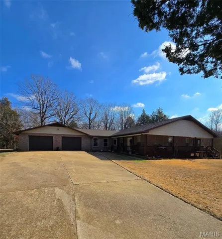 Single story home with driveway, covered porch, brick siding, and an attached garage