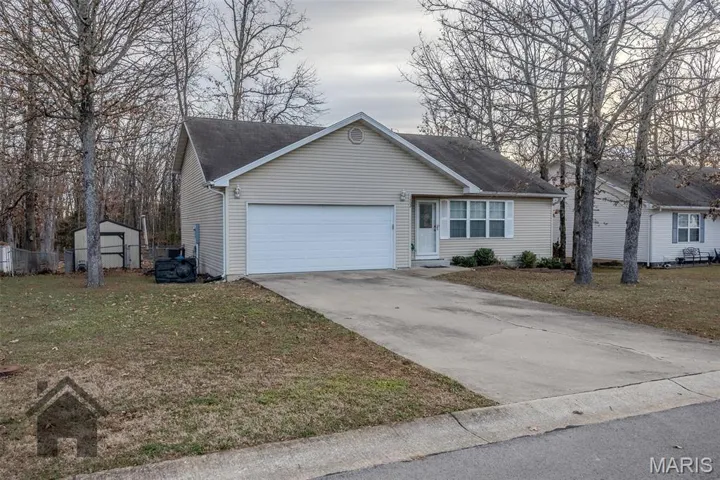 Ranch-style home featuring a front yard, driveway, a garage, and a shed