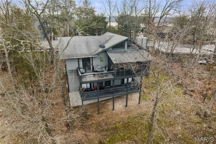 Rear view of property featuring a wooden deck, a shingled roof, a chimney, and view of wooded area