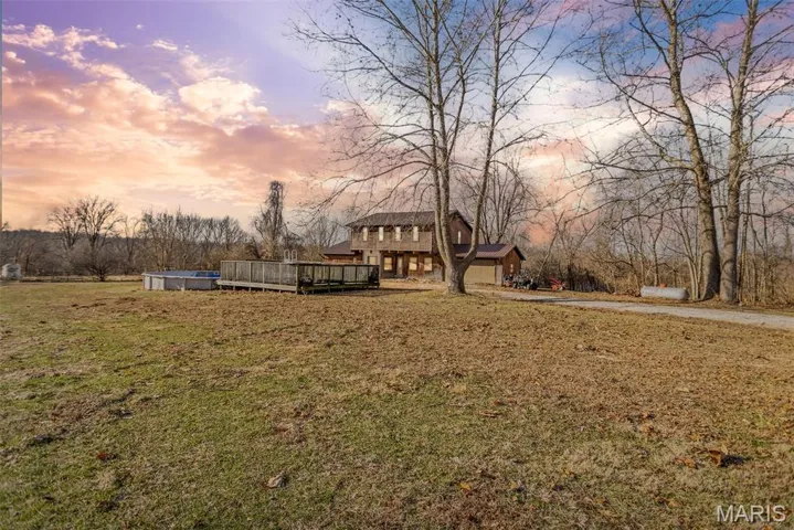 Yard at dusk with driveway, a deck, a yard, a garage, and an outdoor pool
