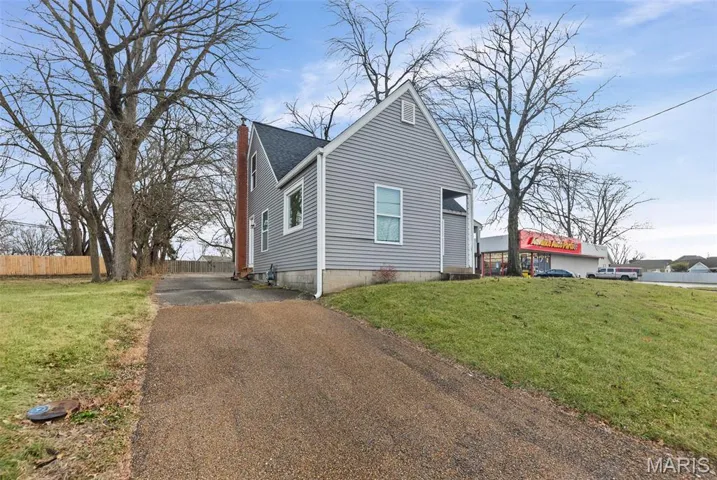 View of side of home featuring asphalt driveway, a shingled roof, and a chimney