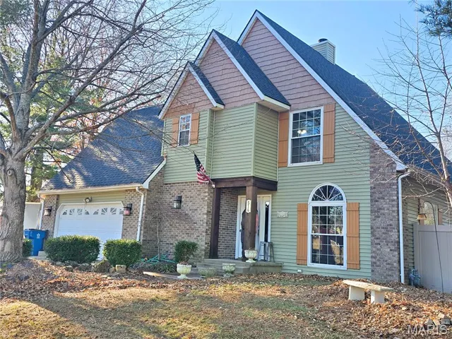 Traditional-style home with a shingled roof, a chimney, an attached garage, and brick/vinyl  siding