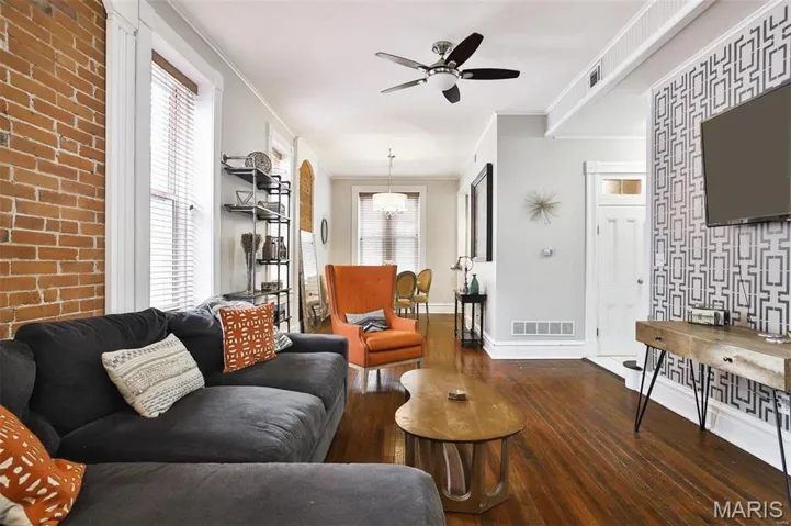 Living room with dark wood-type flooring, an accent wall, crown molding, healthy amount of natural light, and ceiling fan