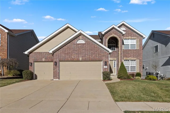 Traditional-style home featuring brick siding, driveway, an attached garage, and a front lawn