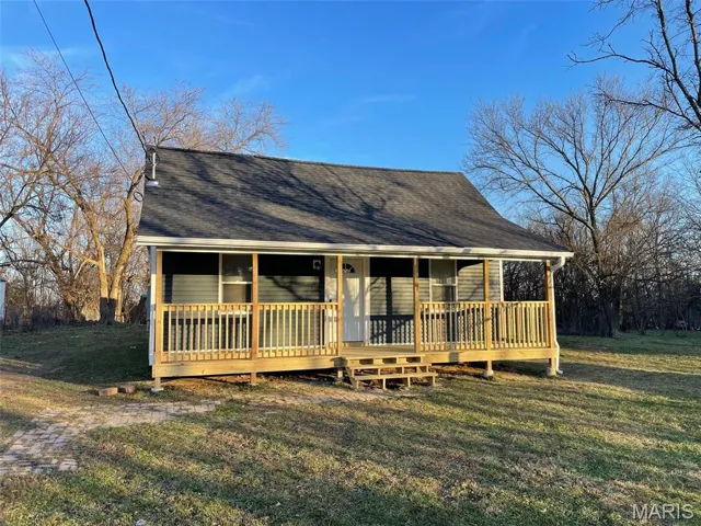 View of front facade with a front lawn, roof with shingles, and covered porch