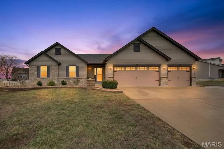 View of front facade with stone siding, concrete driveway, a front yard, and a garage