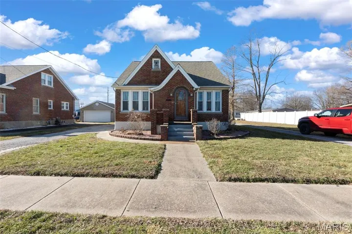 View of front facade featuring brick siding, roof with shingles, and a detached garage