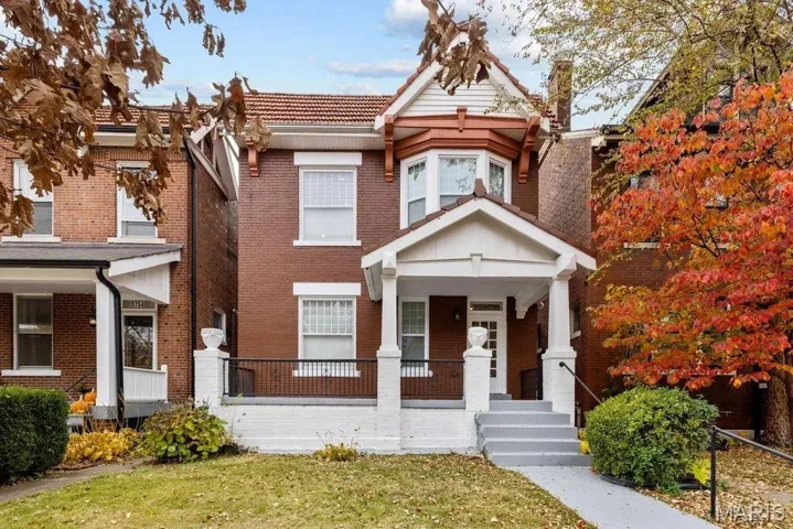 View of front facade with a porch, a front lawn, brick siding, and a tiled roof