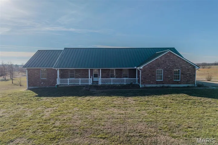View of front facade featuring brick siding, covered porch, a metal roof, and a standing seam roof