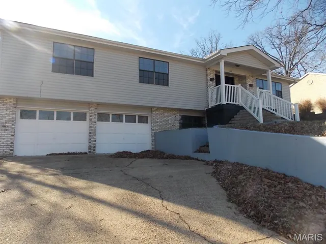 View of front of home with brick siding, driveway, a garage, and covered porch