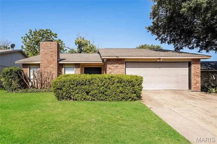 Single story home featuring a shingled roof, brick siding, driveway, a front lawn, and a chimney