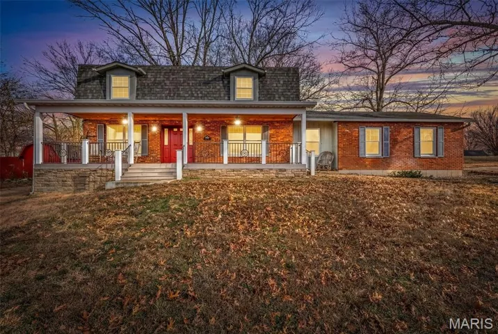 View of front of home featuring covered porch, brick siding, roof with shingles, and a yard