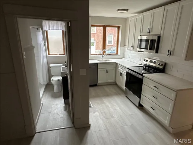 Kitchen with stainless steel appliances, white cabinetry, tasteful backsplash, and light stone countertops