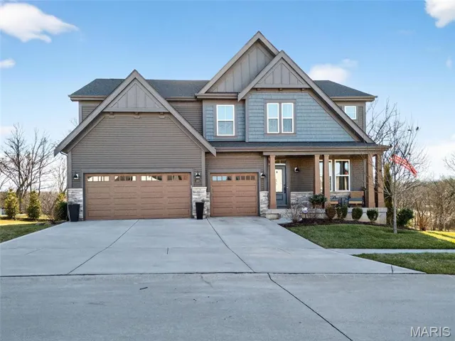 Craftsman-style house with concrete driveway, stone siding, a front lawn, board and batten siding, and covered porch