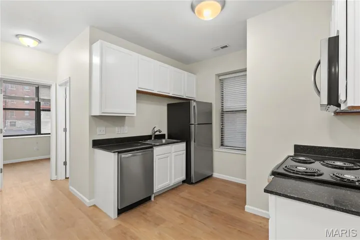Kitchen featuring white cabinets, stainless steel appliances, light wood finished floors, and dark stone countertops