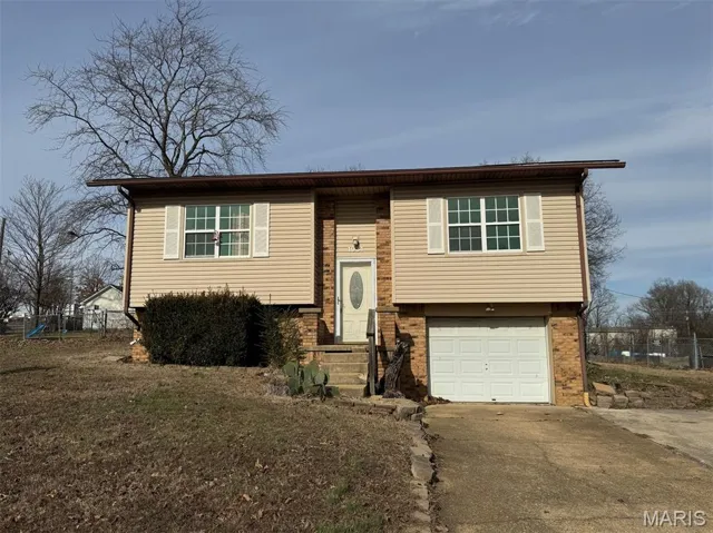 Raised ranch featuring an attached garage, concrete driveway, and brick siding