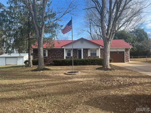 Single story home featuring brick siding, a metal roof, driveway, an attached garage, and a front yard