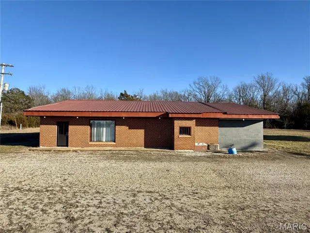 Back of house with a metal roof and brick siding