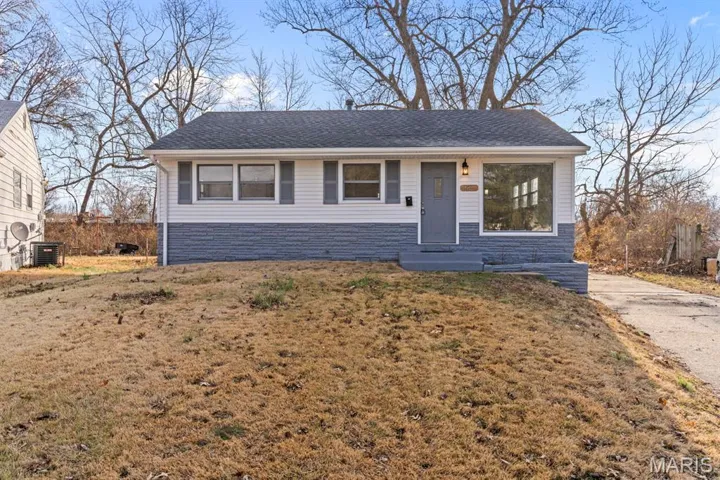 View of front of property featuring a shingled roof, stone siding, and a front yard