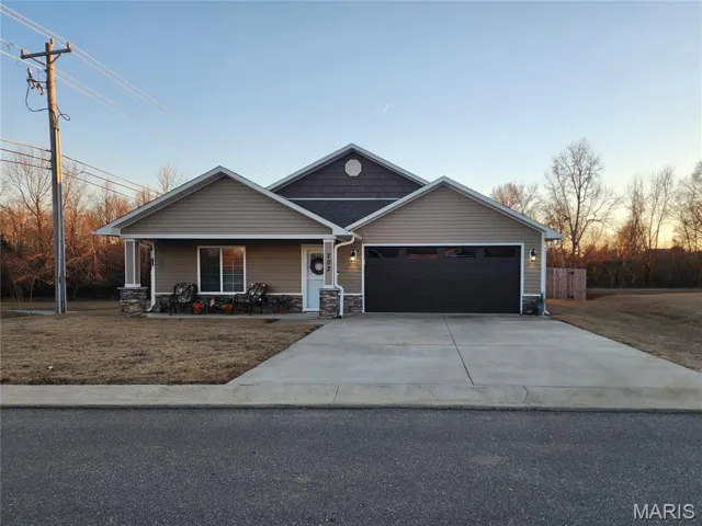 Craftsman-style home featuring a porch, driveway, stone siding, and a garage
