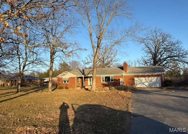Ranch-style home with driveway, a chimney, an attached garage, and brick siding