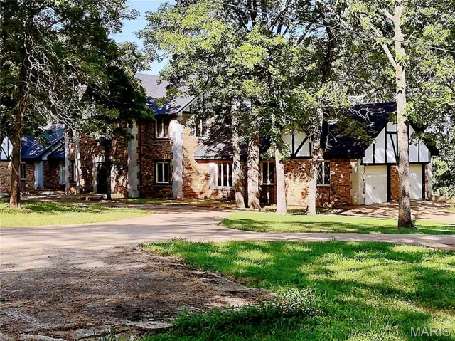 English style home featuring brick siding, a front yard, driveway, and a garage