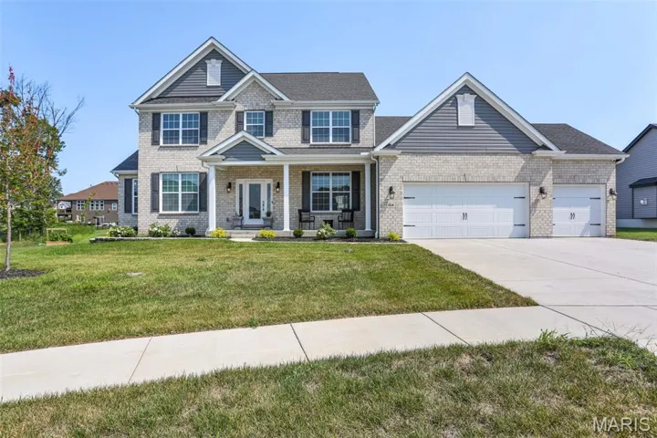 View of front of home featuring a front lawn, brick siding, driveway, an attached garage, and covered porch