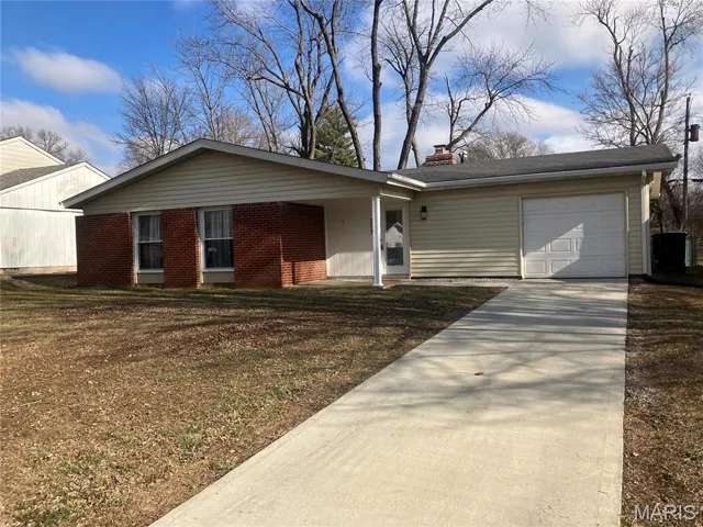 Ranch-style house featuring a chimney, an attached garage, brick siding, concrete driveway, and a front lawn
