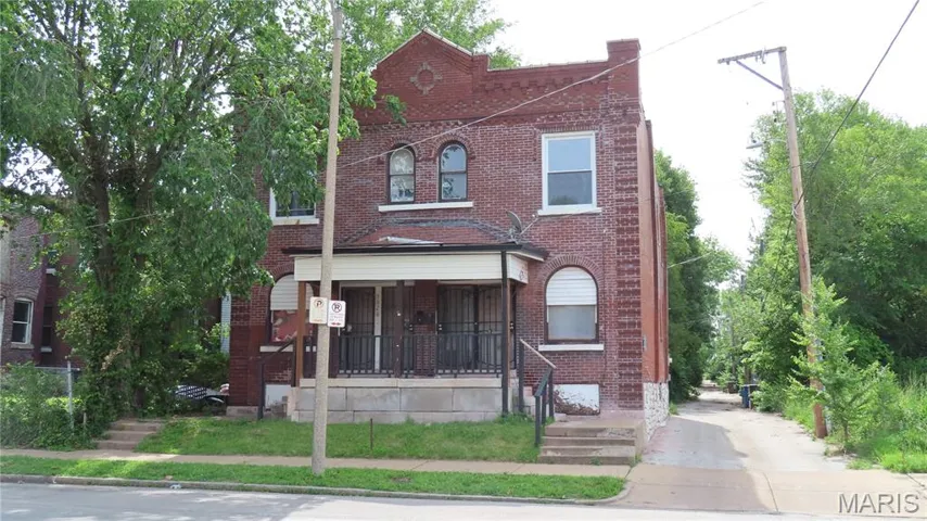 View of property featuring brick siding, driveway, and covered porch