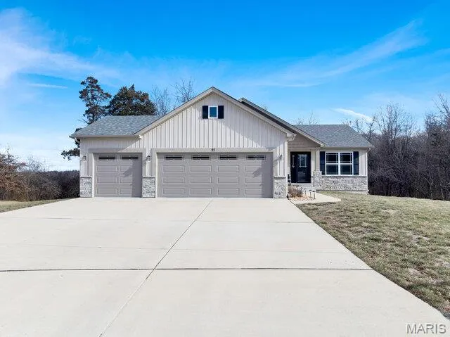 View of front facade featuring stone siding, driveway, a garage, and a front lawn