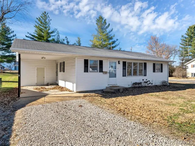 Single story home featuring a carport, gravel driveway, entry steps, and a front lawn