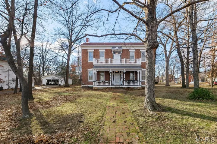 Italianate house with covered porch, a chimney, a front lawn, brick siding, and an outbuilding