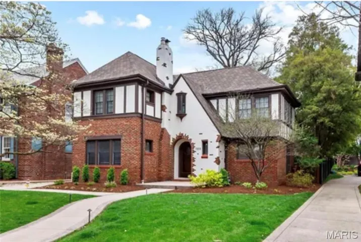 Tudor home featuring a front lawn, a chimney, and brick siding