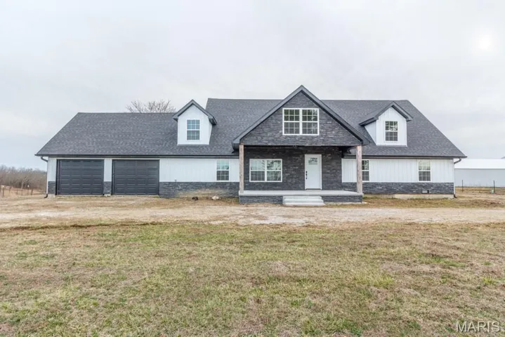 View of front of property featuring a porch, a front lawn, a garage, driveway, and stone siding