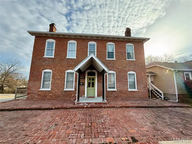 Front of building, shows large windows, brick building and brick paver area.