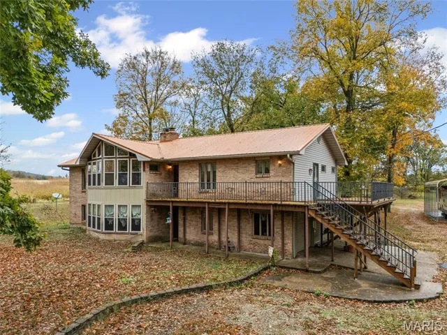 Back of house featuring a chimney, stairs, brick siding, a wooden deck, and a patio